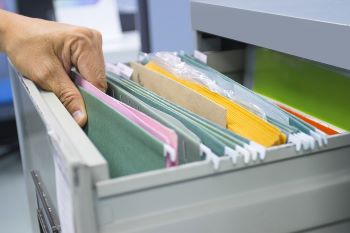 Closeup of a person's hand pulling a hanging file out of a filing cabinet drawer.