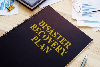 A notebook sitting on a desk. The notebook is labelled Disaster Recovery Plan.