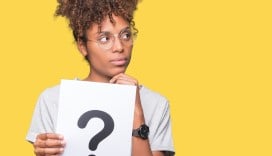 A person thinking while holding up a piece of paper with a question mark printed on it