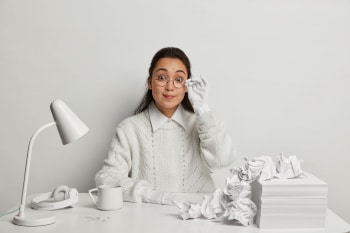 A person sitting at a messy desk. Everything on the desk and that the person is wearing is the same shade of white