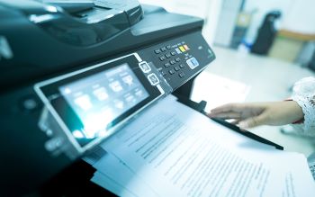 Business documents coming out of an office scanner and a woman's hand is shown removing the documents