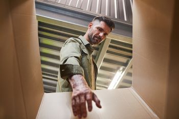 Low angle point of view shot at bearded man carrying box while loading self storage unit