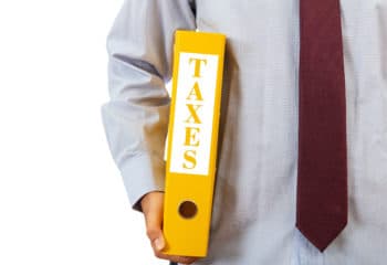 A person wearing a tie holding a yellow binder labelled "Taxes"