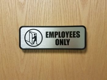 A silver and black employees only sign on wood door