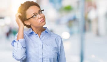 A young business professional looking confused standing in front of a blurred street background.