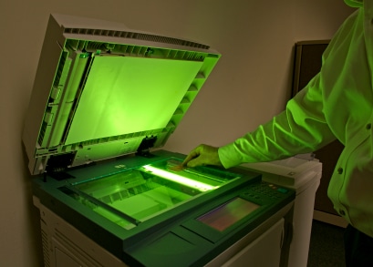 A person placing an item on an open photocopier with a green neon light shining out of it